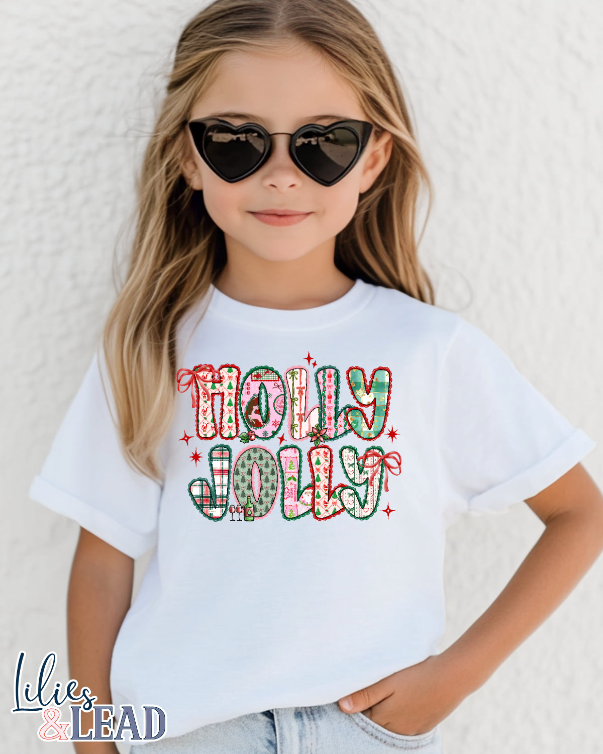 Child wearing a white t-shirt with 'Holly Jolly' text, sunglasses, and jeans on a light background.