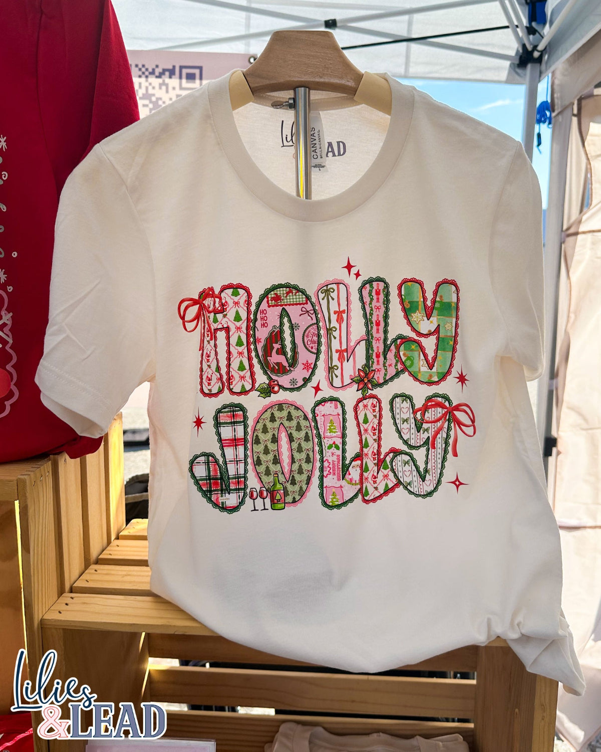 White t-shirt with 'Holly Jolly' text on a wooden rack.