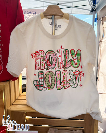 White t-shirt with 'Holly Jolly' text on a wooden rack.