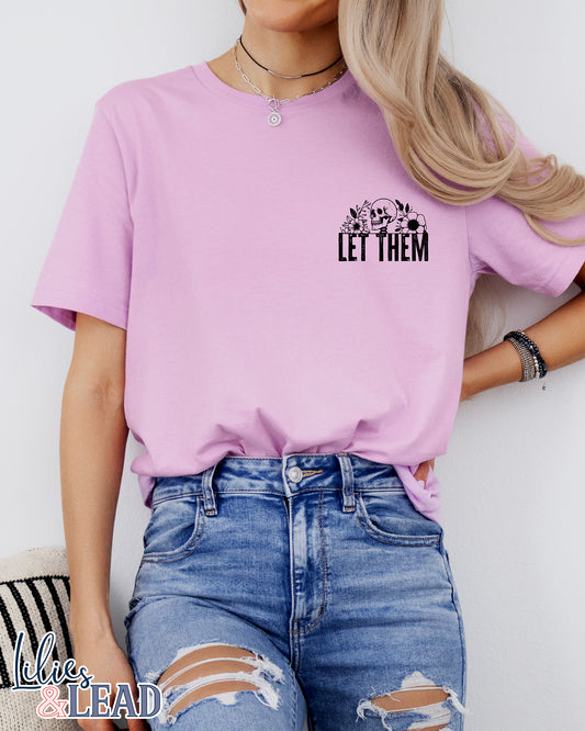 Lilac short sleeve tee featuring a pocket area design with black skeleton and florals and the saying "Let Them"