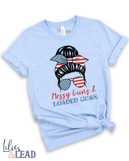 light blue tee shirt  flatlay with messy buns design wearing patriotic bandana and sunglasses featuring the phrase Messy buns and loaded guns 
