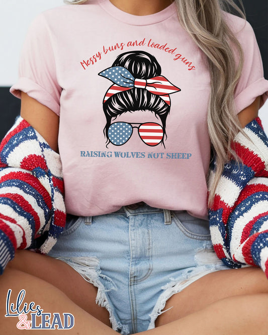 Soft pink tee shirt  on model with messy buns design wearing patriotic bandana and sunglasses featuring the phrase Messy buns and loaded guns raising wolves not sheep