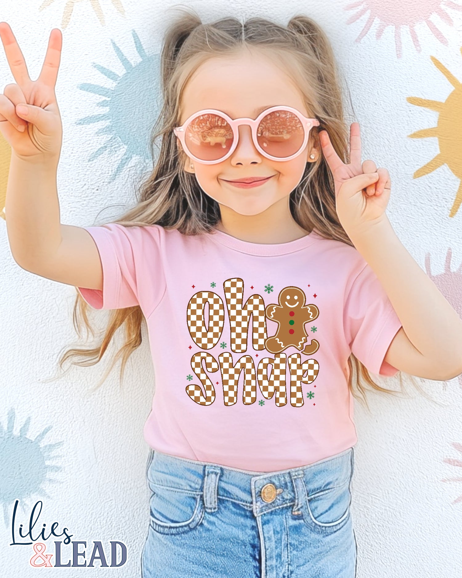 Child wearing a pink t-shirt with Oh Snap' design and denim shorts, posing with peace signs.