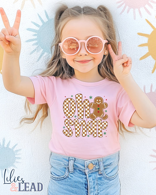 Child wearing a pink t-shirt with Oh Snap' design and denim shorts, posing with peace signs.