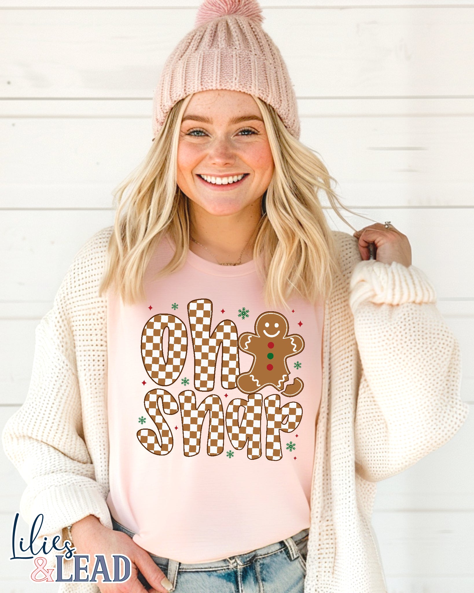 Woman wearing a pink shirt with 'Oh Snap' gingerbread design and a pink beanie against a white background.