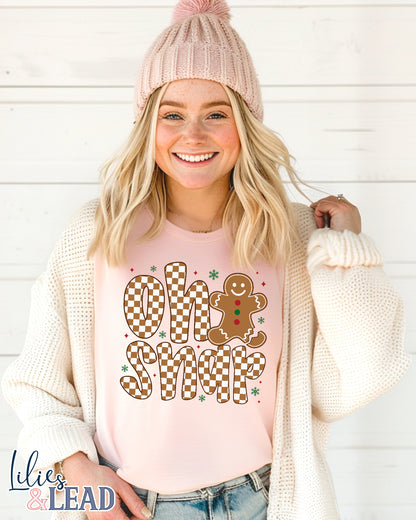 Woman wearing a pink shirt with 'Oh Snap' gingerbread design and a pink beanie against a white background.